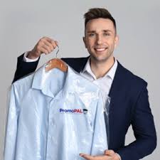 Male in navy suit holding up a PromoPAL branded pale blue button up shirt with a grey background