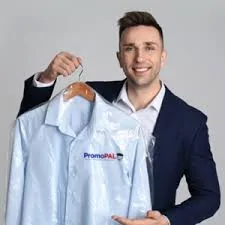 Male in navy suit holding up a PromoPAL branded pale blue button up shirt with a grey background