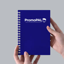 Royal blue notepad with PromoPAL logo being held with two hands and a grey background