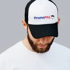 Male with beard and white shirt wearing a white and black cap with PromoPal branding and a grey background